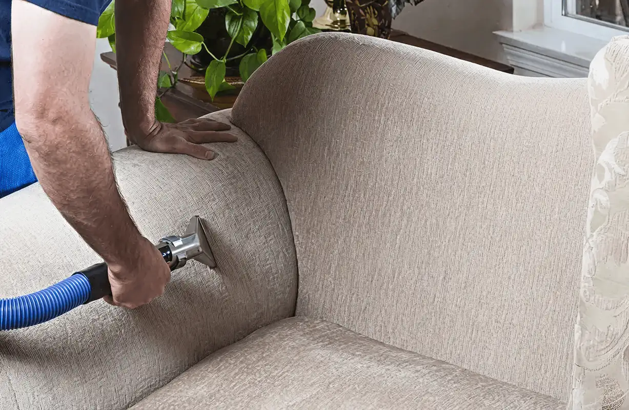 Professional upholstery cleaner deep-cleaning a fabric sofa with a handheld extraction tool and hose, Los Angeles, CA.